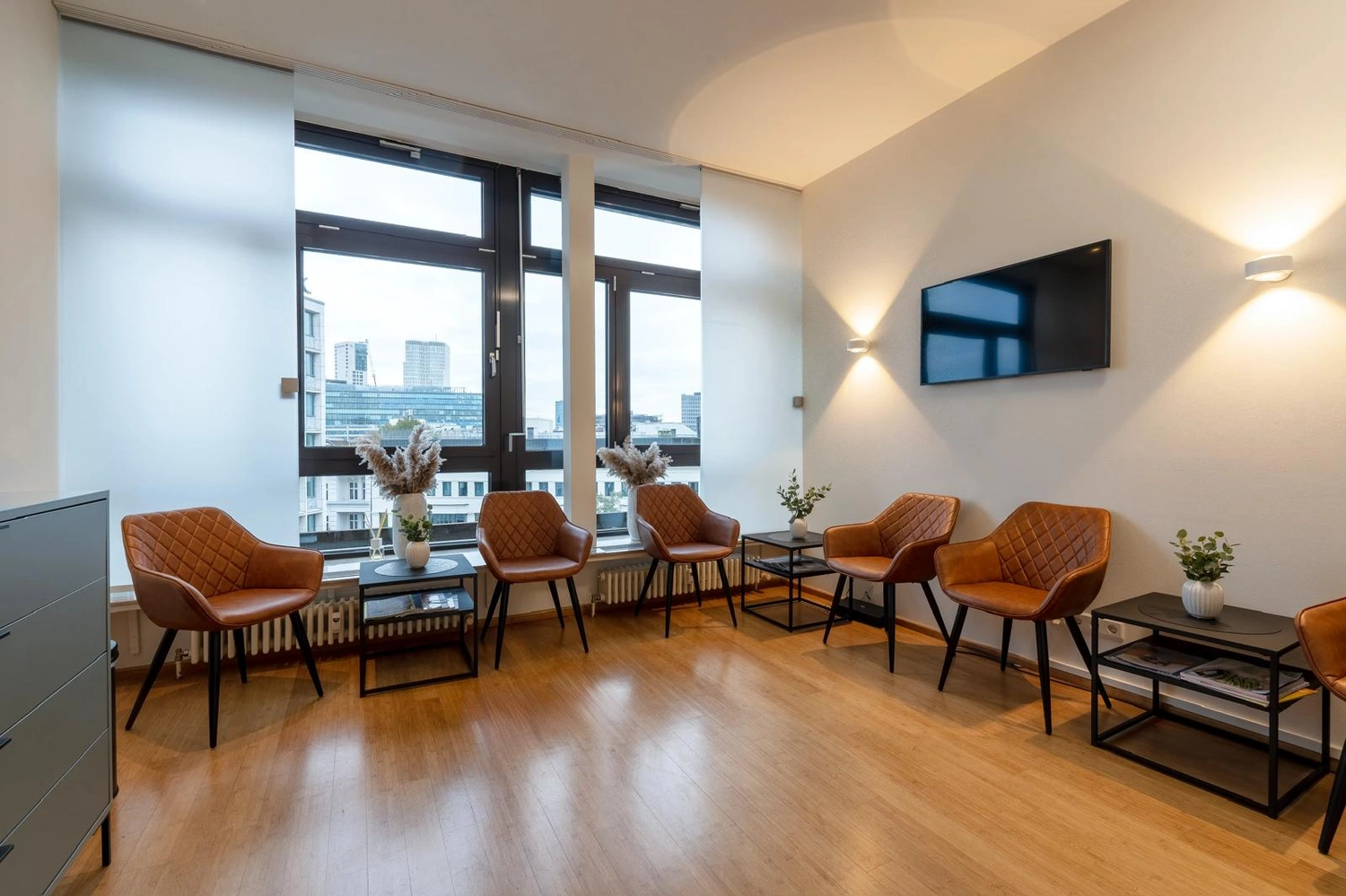 Flink Mediclean - Hygienische Reinigung für medizinische & therapeutische Einrichtungen - Ein helles, modernes Wartezimmer mit mehreren hellbraunen, rautenförmig gesteppten Ledersesseln vor weißen Wänden und großen Fenstern, ergänzt durch minimalistische schwarze Beistelltische und warme Wandbeleuchtung.