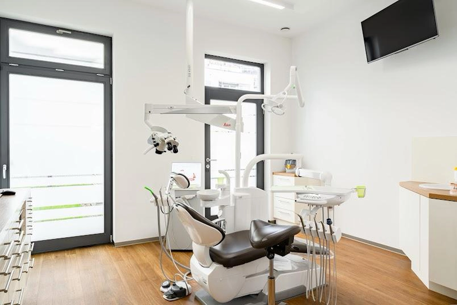 Flink Mediclean - Hygienische Reinigung für medizinische & therapeutische Einrichtungen - Ein moderner Zahnarztbehandlungsraum mit einem eleganten weißen Behandlungsstuhl, fortschrittlicher Deckenbeleuchtung, einem Dentalmikroskop und integrierten digitalen Displays in einem hellen, minimalistischen Raum mit Holzboden.